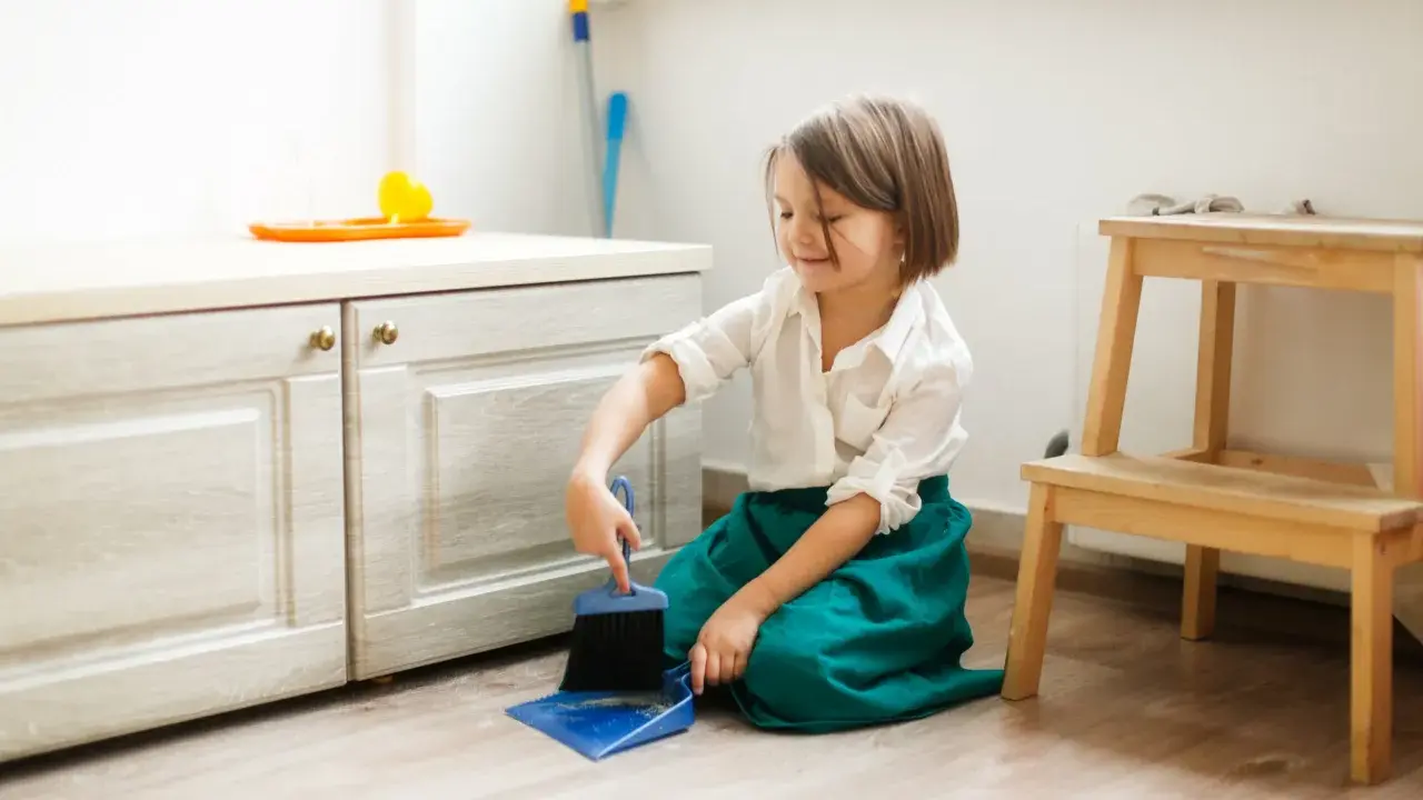 Niña practicando vida práctica Montessori, barriendo el suelo con escoba y recogedor.