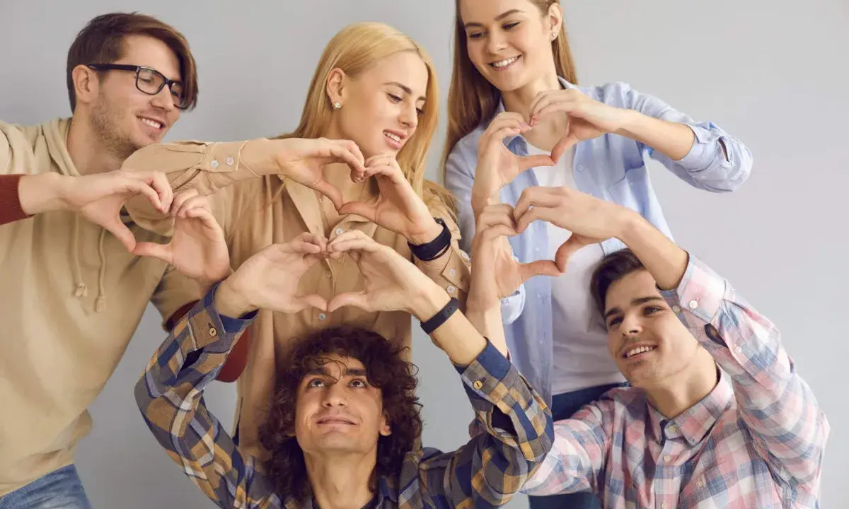 Cinco jóvenes sonríen formando corazones con sus manos, un gesto que puede servir como frases enseñar sobre la amistad y el amor.