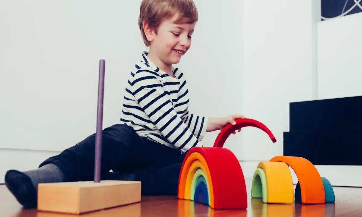 Niño sonriente juega con bloques de madera de arcoíris, un ejemplo de la pedagogía Waldorf que fomenta la creatividad y el desarrollo.