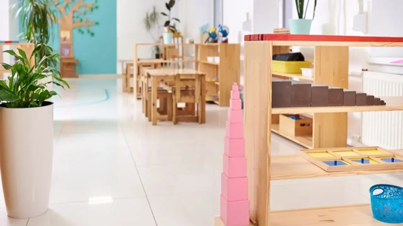 Un aula Montessori 0-3 años con mesas bajas, estanterías de madera y materiales didácticos como la torre rosa.