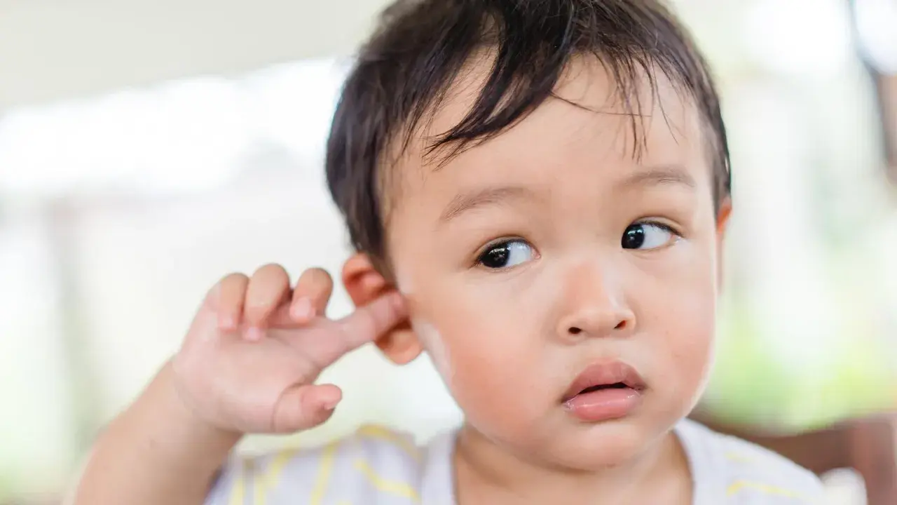 Niño asiático se mete el dedo en la oreja, quizás para quitarse la suciedad detrás de las orejas.