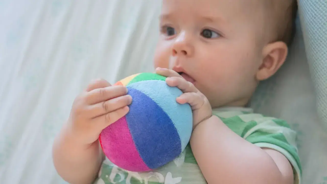 Bebé explorando el mundo con su sentido tacto, agarrando una pelota de colores.