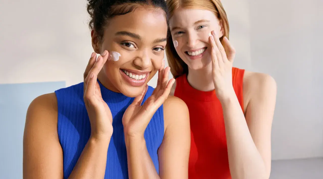 Dos mujeres sonríen mientras aplican crema en sus rostros. Piel con piel hasta cuando, la belleza natural se realza con cuidado.