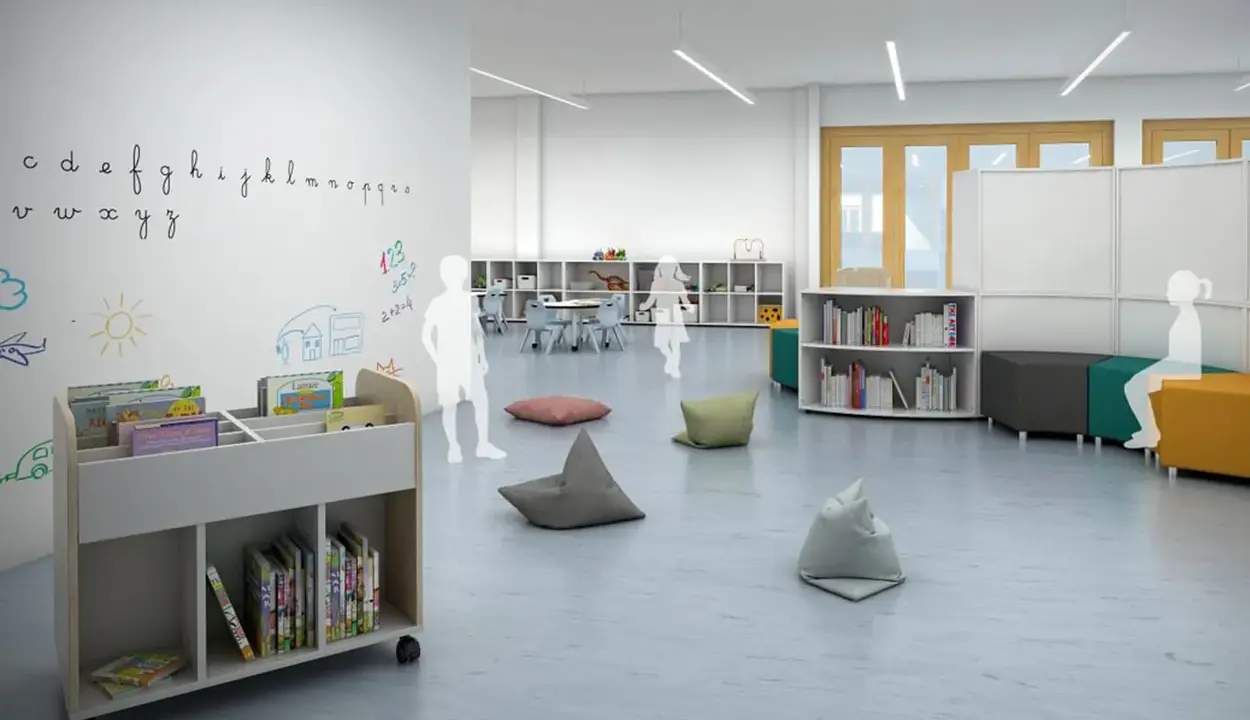 Plano de aula infantil con estanterías, libros, pufs y dibujos en la pared.