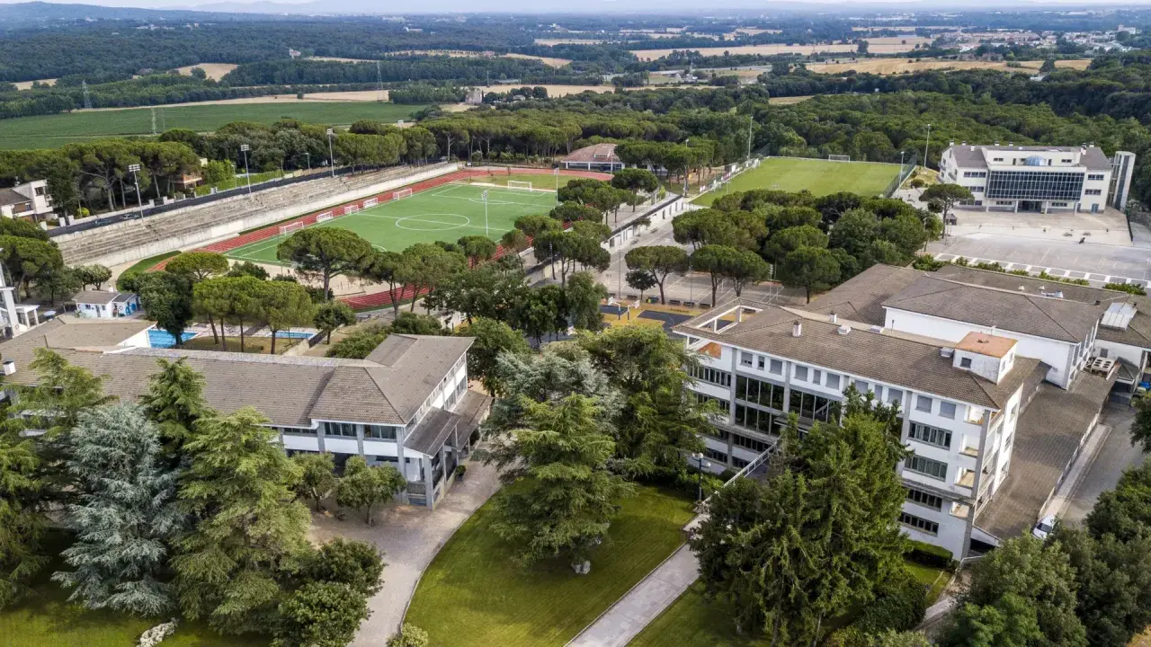 Vista aérea de un colegio Montessori con campos deportivos, piscina y edificios modernos rodeados de árboles.