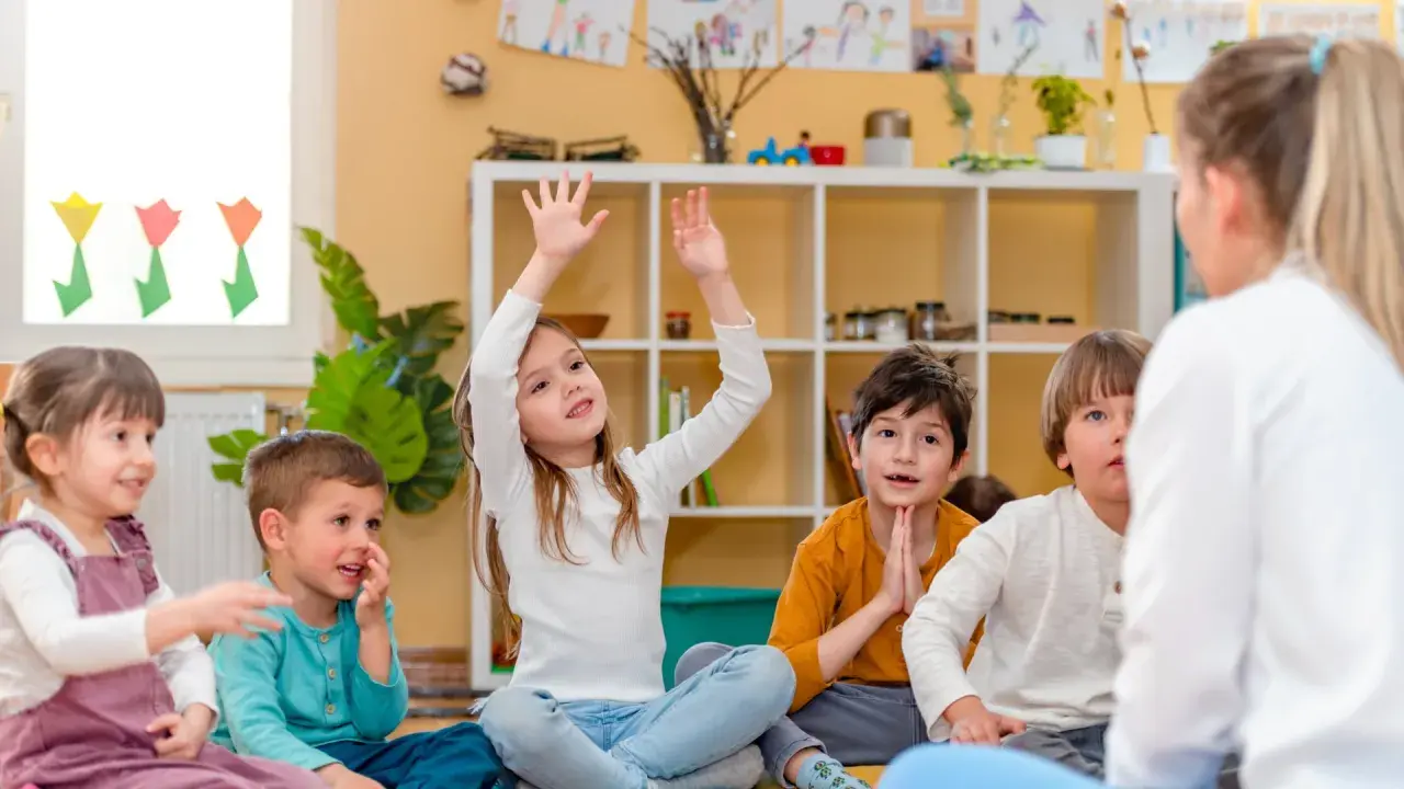 Niños atentos en clase, quizás buscando frases para profesores despedida. Una niña levanta la mano, ansiosa por participar.