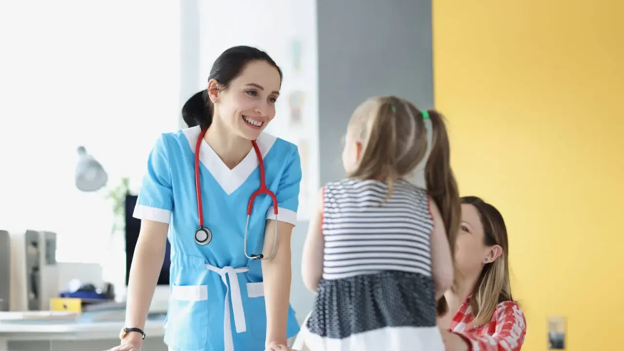 Doctora sonríe a niña y madre, ofreciendo atención educativa en un entorno médico.