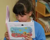 Niña leyendo un libro ilustrado, parte de una colección de libros por edades.
