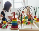 Juguetes de madera coloridos, como un cochecito de pato y un ábaco, forman parte de una guía Montessori para el aprendizaje infantil.
