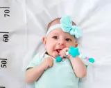 Un bebé sonriente con un chupete de estrella turquesa, con una cinta azul en la cabeza. A su lado, una regla marca el crecimiento, ¡un bebé perceptible!