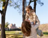Madre levanta a su hija riendo, un momento lleno de palabras bonitas para niños y amor en un día soleado en el parque.