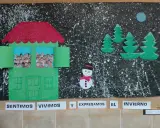 Decoración invierno aula infantil: una casa verde con fotos de niños, árboles, muñeco de nieve y luna sobre fondo negro salpicado.