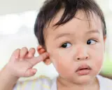 Niño asiático se mete el dedo en la oreja, quizás para quitarse la suciedad detrás de las orejas.