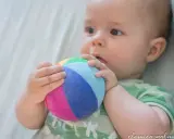 Bebé explorando el mundo con su sentido tacto, agarrando una pelota de colores.