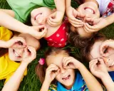 Niños riendo y jugando en el césped, creando formas con sus manos. Sonrisas contagiosas, perfectas para frases para niños.