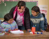 Maestra ayuda a dos niñas en un aula, promoviendo la importancia de las escuelas inclusivas.