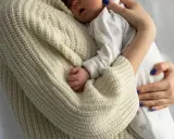 Bebé durmiendo acurrucado en brazos de su madre, envuelto en un suéter tejido. Un recordatorio de cuanto duerme un recién nacido.