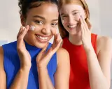 Dos mujeres sonríen mientras aplican crema en sus rostros. Piel con piel hasta cuando, la belleza natural se realza con cuidado.