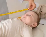 Bebé de 20 meses siendo medido con cinta métrica. Un peluche de conejo observa atentamente.