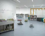 Plano de aula infantil con estanterías, libros, pufs y dibujos en la pared.