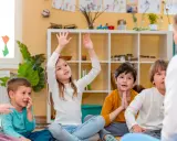 Niños atentos en clase, quizás buscando frases para profesores despedida. Una niña levanta la mano, ansiosa por participar.