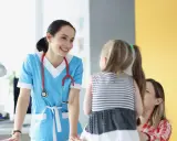 Doctora sonríe a niña y madre, ofreciendo atención educativa en un entorno médico.