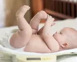 Bebé en báscula, con las piernas en alto. Su peso podría estar en el percentil 90, indicando un buen desarrollo.