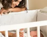 Madre sonríe a su bebé en la cuna. Un momento tierno para empezar a enseñar a un bebé a enlazar ciclos de sueño.