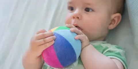 Bebé explorando el mundo con su sentido tacto, agarrando una pelota de colores.