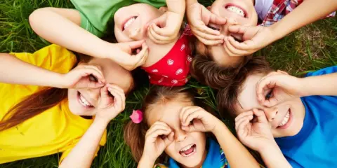 Niños riendo y jugando en el césped, creando formas con sus manos. Sonrisas contagiosas, perfectas para frases para niños.