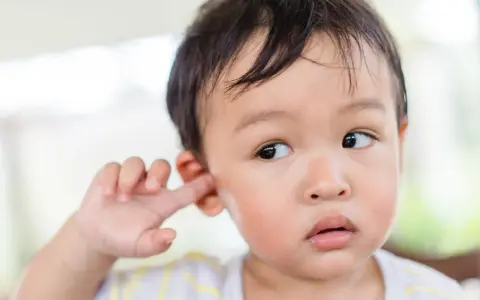 Niño asiático se mete el dedo en la oreja, quizás para quitarse la suciedad detrás de las orejas.