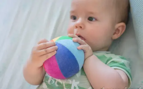 Bebé explorando el mundo con su sentido tacto, agarrando una pelota de colores.