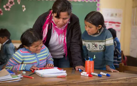 Maestra ayuda a dos niñas en un aula, promoviendo la importancia de las escuelas inclusivas.