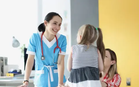 Doctora sonríe a niña y madre, ofreciendo atención educativa en un entorno médico.