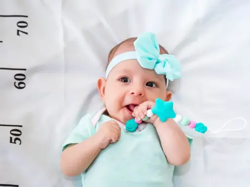 Un bebé sonriente con un chupete de estrella turquesa, con una cinta azul en la cabeza. A su lado, una regla marca el crecimiento, ¡un bebé perceptible!