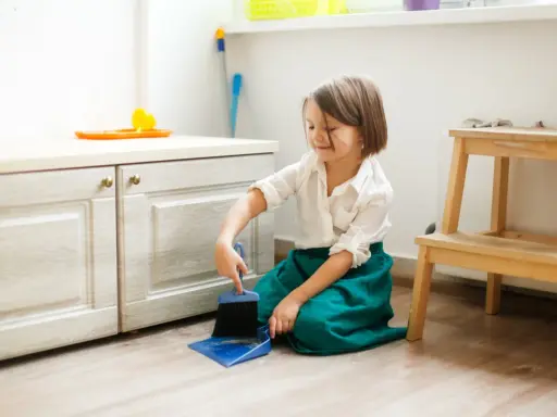 Niña practicando vida práctica Montessori, barriendo el suelo con escoba y recogedor.