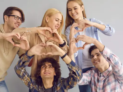 Cinco jóvenes sonríen formando corazones con sus manos, un gesto que puede servir como frases enseñar sobre la amistad y el amor.
