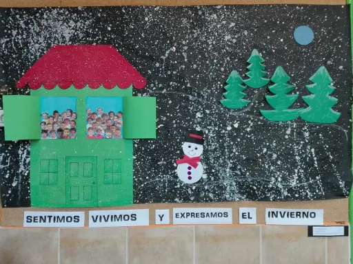 Decoración invierno aula infantil: una casa verde con fotos de niños, árboles, muñeco de nieve y luna sobre fondo negro salpicado.