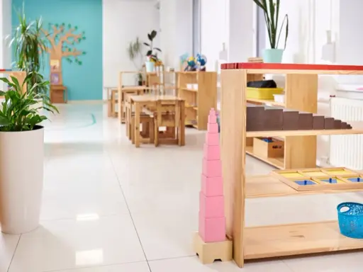 Un aula Montessori 0-3 años con mesas bajas, estanterías de madera y materiales didácticos como la torre rosa.