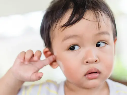Niño asiático se mete el dedo en la oreja, quizás para quitarse la suciedad detrás de las orejas.