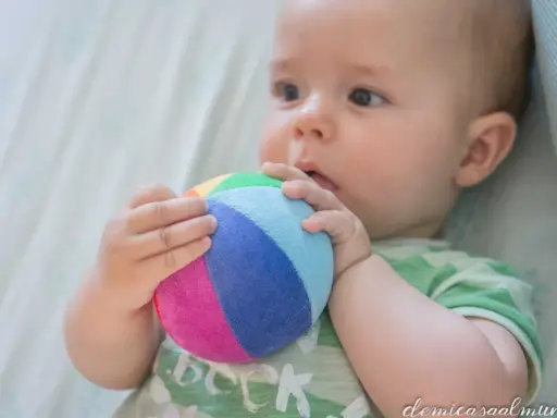 Bebé explorando el mundo con su sentido tacto, agarrando una pelota de colores.