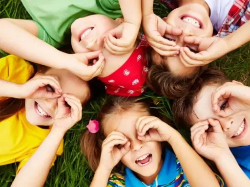 Niños riendo y jugando en el césped, creando formas con sus manos. Sonrisas contagiosas, perfectas para frases para niños.