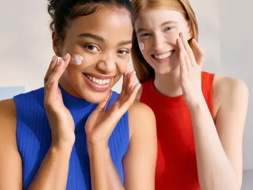 Dos mujeres sonríen mientras aplican crema en sus rostros. Piel con piel hasta cuando, la belleza natural se realza con cuidado.