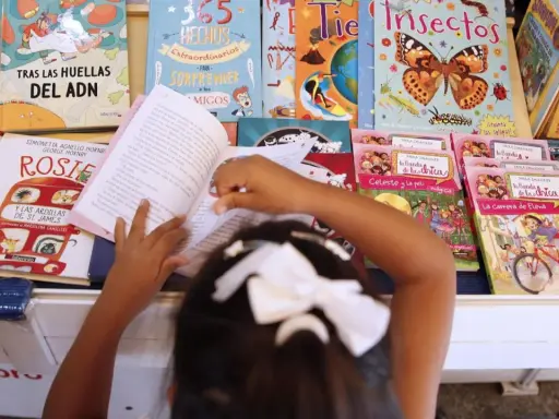 Niña lee libros sobre cuentos de igualdad de género, rodeada de coloridas portadas que inspiran a la imaginación.