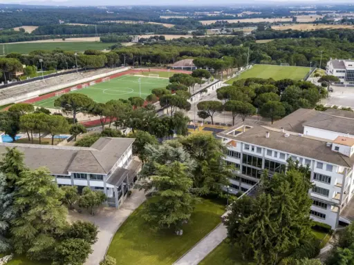 Vista aérea de un colegio Montessori con campos deportivos, piscina y edificios modernos rodeados de árboles.