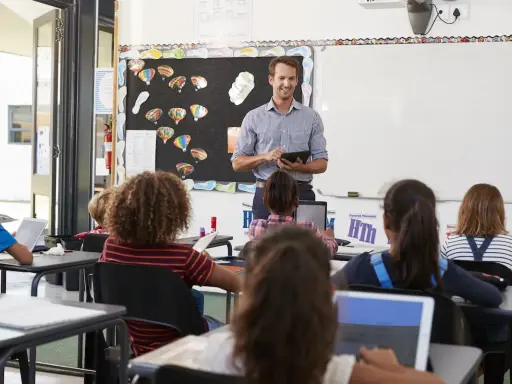Maestro sonriente dirige una clase, los alumnos usan tabletas para su evaluación en casa.