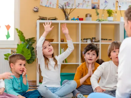Niños atentos en clase, quizás buscando frases para profesores despedida. Una niña levanta la mano, ansiosa por participar.