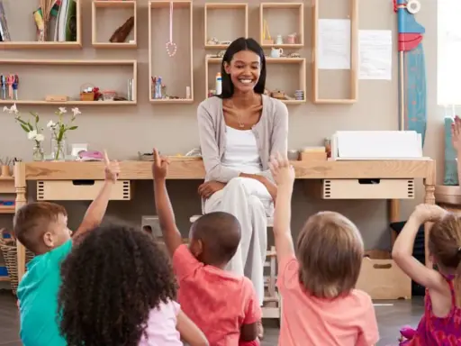 Niños en un aula **Waldorf Montessori** levantan las manos para responder a su maestra sonriente.