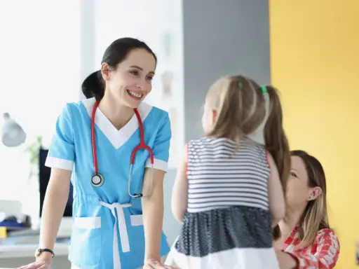 Doctora sonríe a niña y madre, ofreciendo atención educativa en un entorno médico.