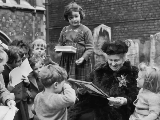 Maria Montessori joven, rodeada de niños, les muestra un libro. Una niña con tirantes sostiene una caja.